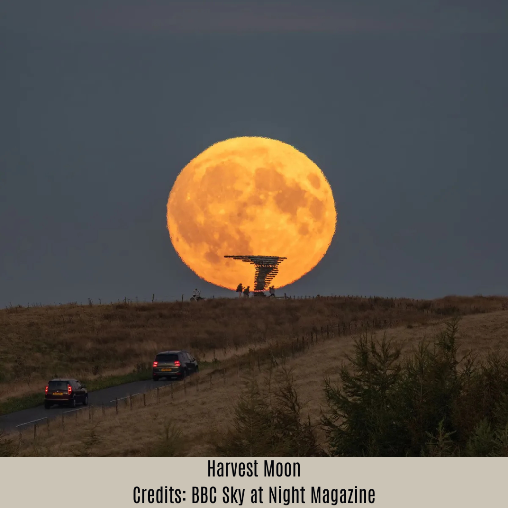 The October Harvest Supermoon appearing large and orange on the horizon, with cars on a road below.
